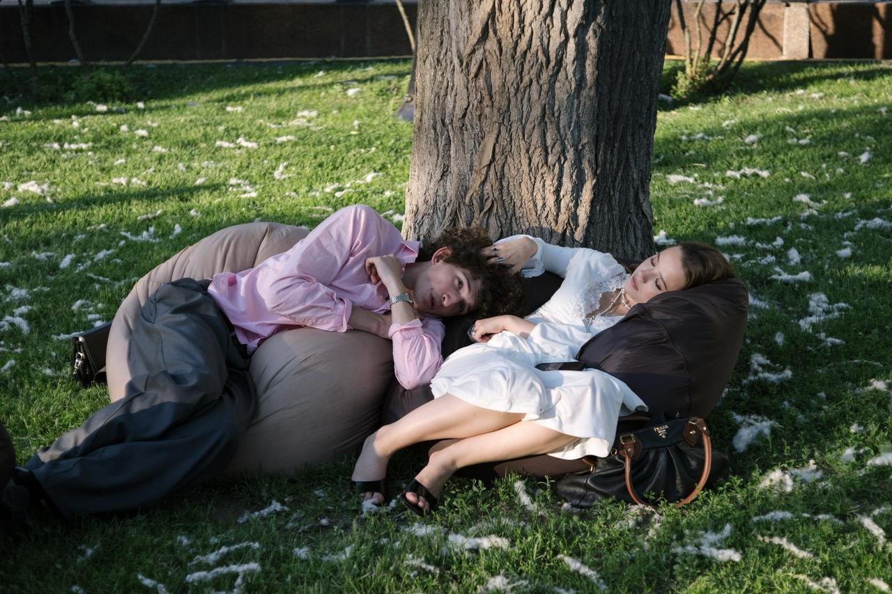 A young man and woman are lying on beanbags under a tree. The woman strokes the man's head, symbolizing the search for a solution following a shared negative sexual experience.